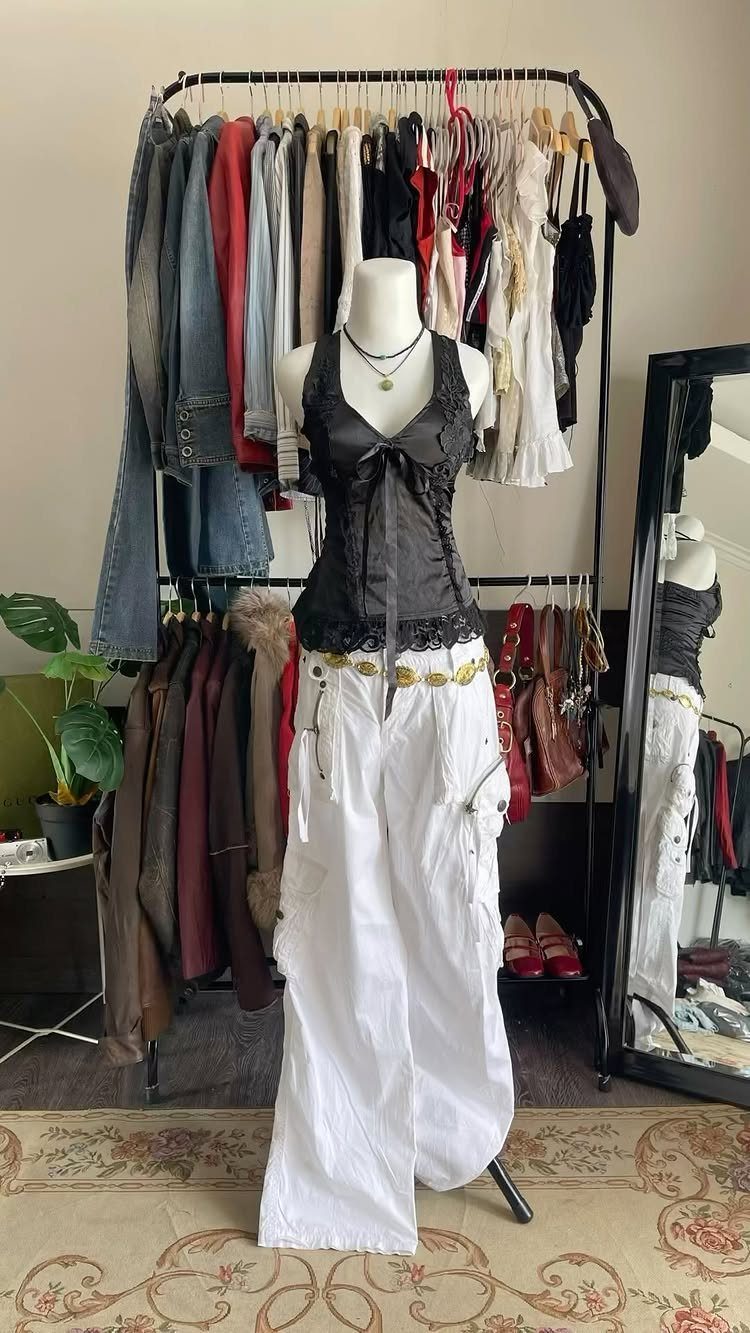 Mannequin wearing a black lace corset and white cargo pants in front of a clothing rack.