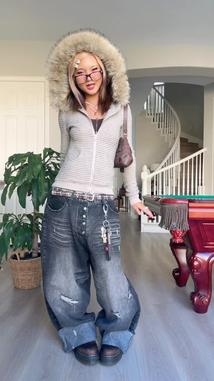A person posing in a grey fur-trimmed hoodie and baggy distressed denim jeans.