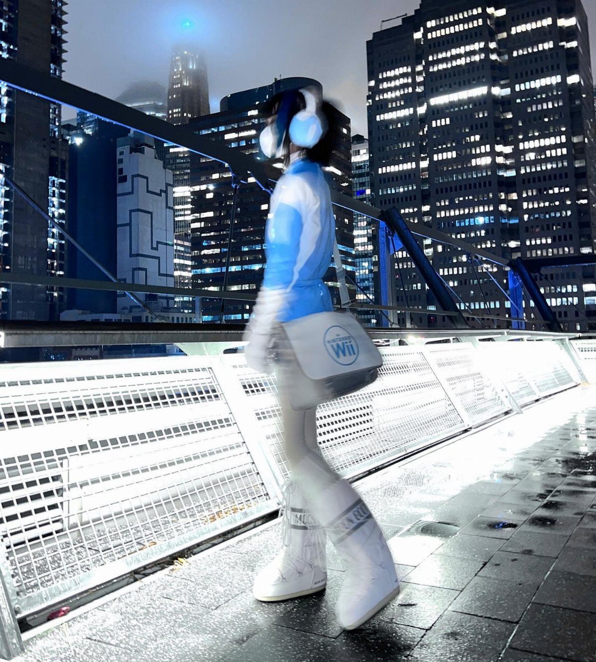 A person in a blue and white futuristic outfit walking across a bridge at night.