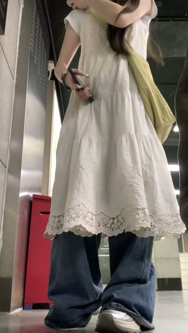A white lace-trimmed tiered dress layered over wide-leg blue denim jeans.