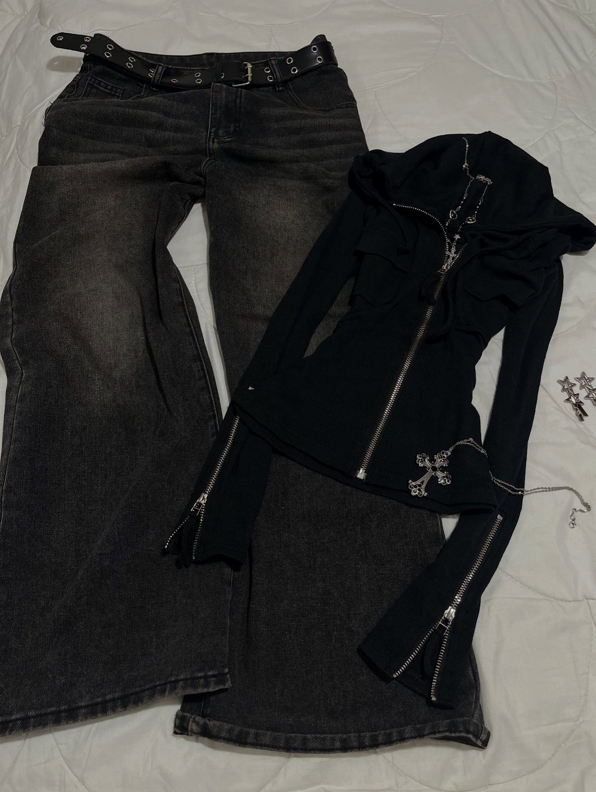 Dark flared jeans with a grommet belt and a black zip-up hoodie laid on white fabric.