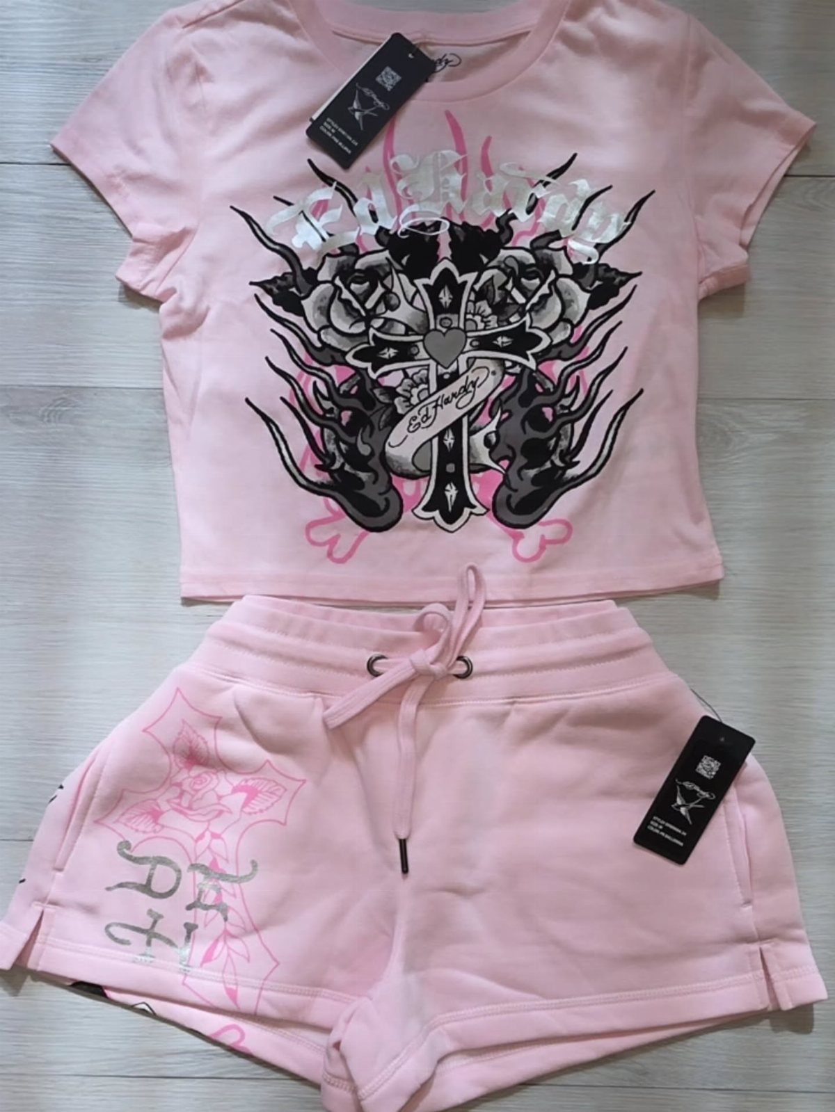 Pink Ed Hardy style baby tee and matching shorts set laid on a light wood surface.