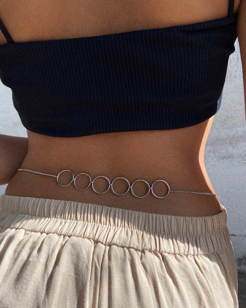 A silver body chain with large circular links resting on a person's waist.