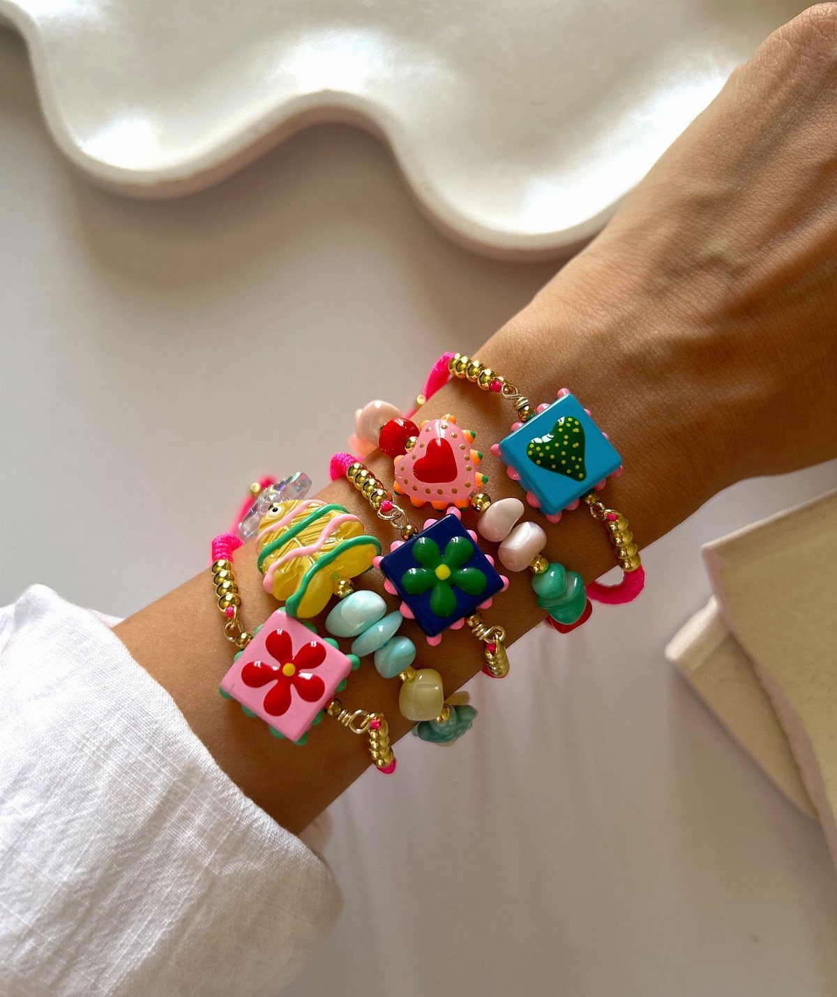 A wrist wearing several bright, colorful beaded bracelets with flower and heart charms.