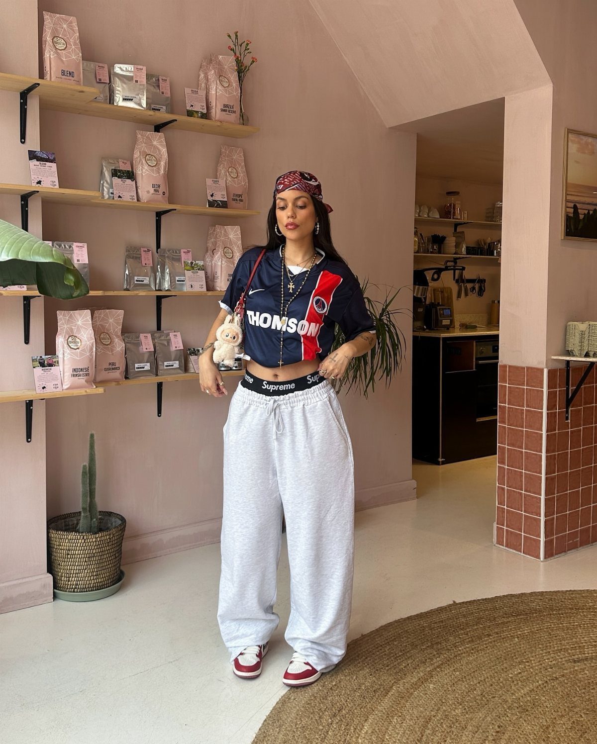 Woman posing in a cafe wearing a cropped black graphic top and baggy grey sweatpants.