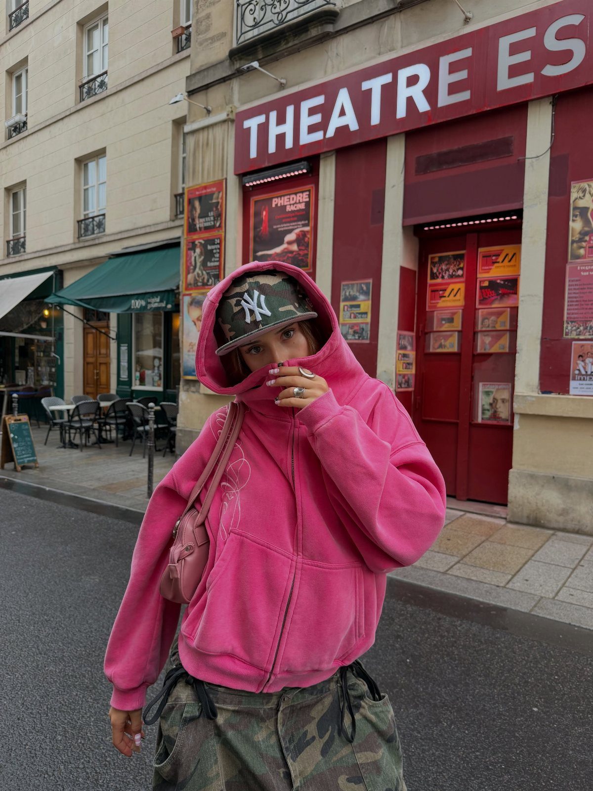 Person in a bright pink hooded sweatshirt and camouflage pants standing on a city street.