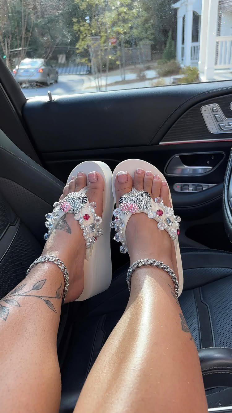 White platform flip-flops decorated with large pearls and pink rhinestones worn on a person's feet.
