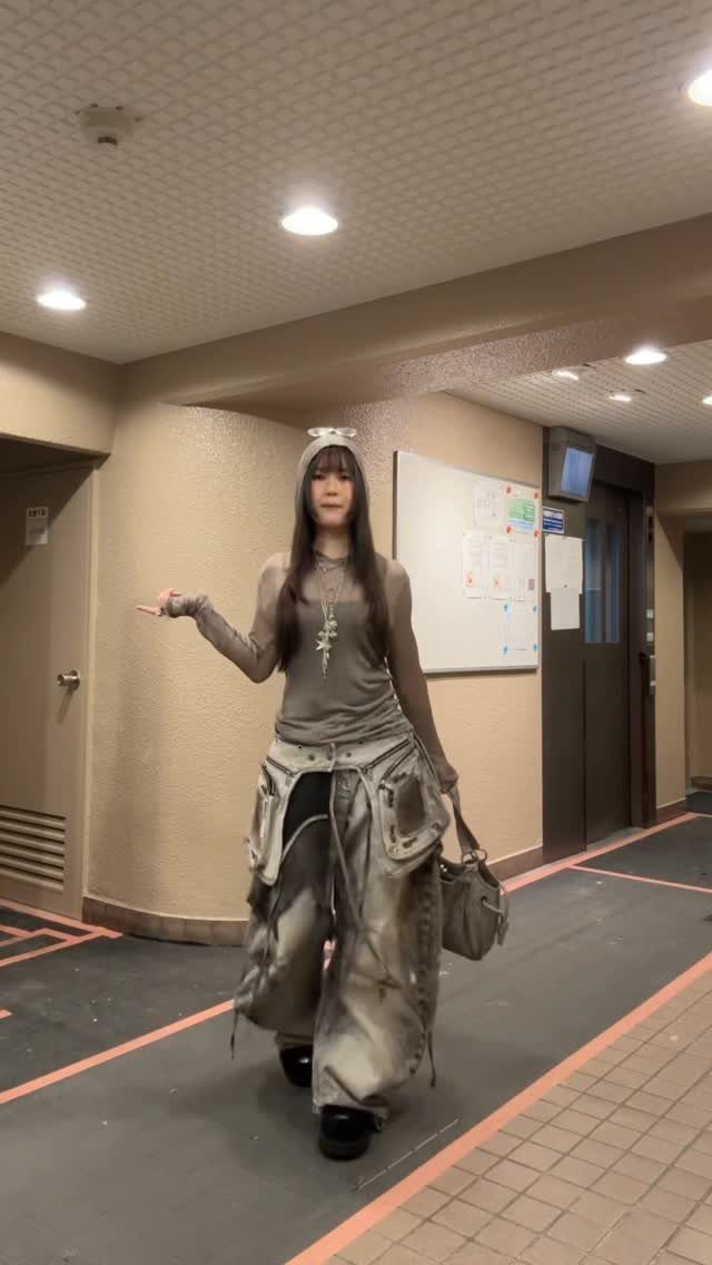 A woman posing in a hallway wearing baggy cargo pants and a sheer grey long-sleeve top.