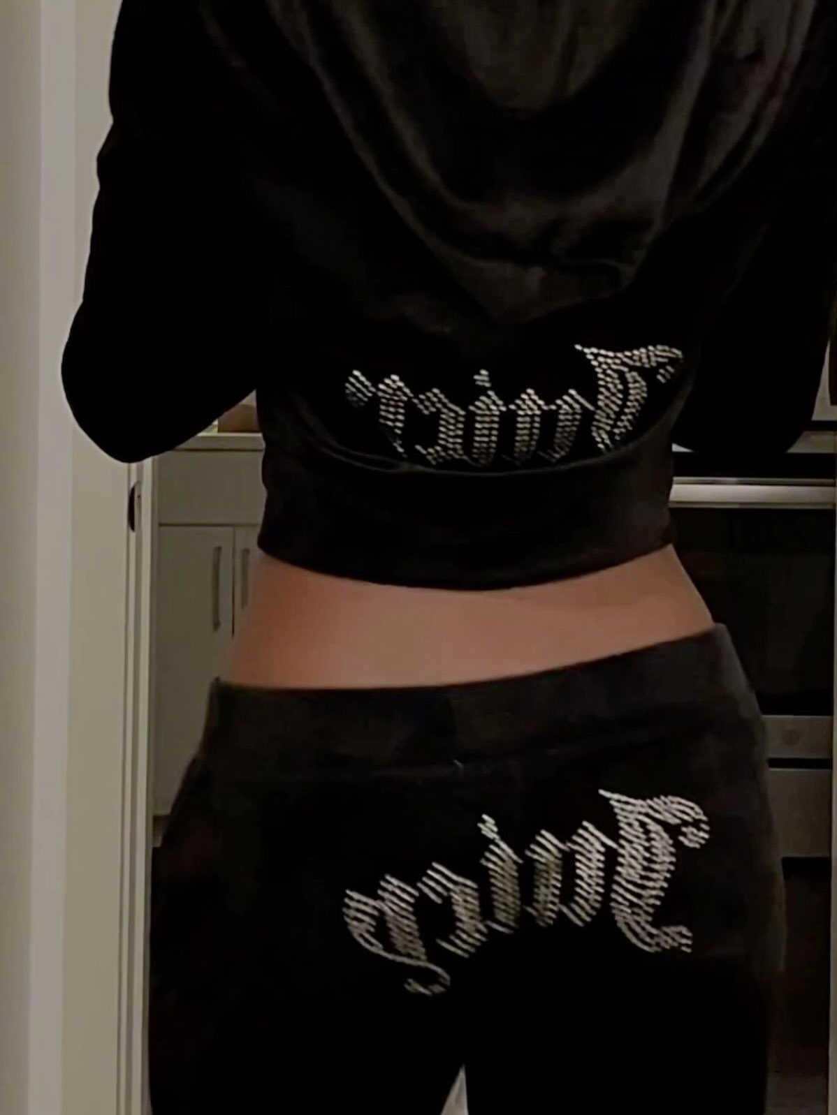 Person wearing a black velour tracksuit with rhinestone Juicy branding on the back.